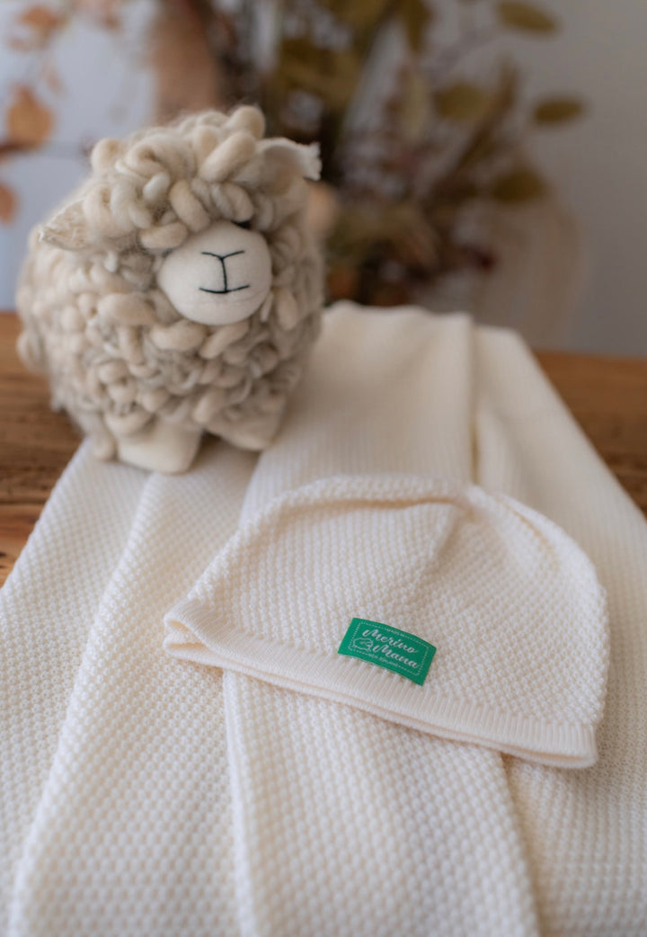 A cream coloured merino wool baby gift, beanie and blanket with a textured moss stitch pattern  A toy sheep made from wool. All items made in New Zealand. 