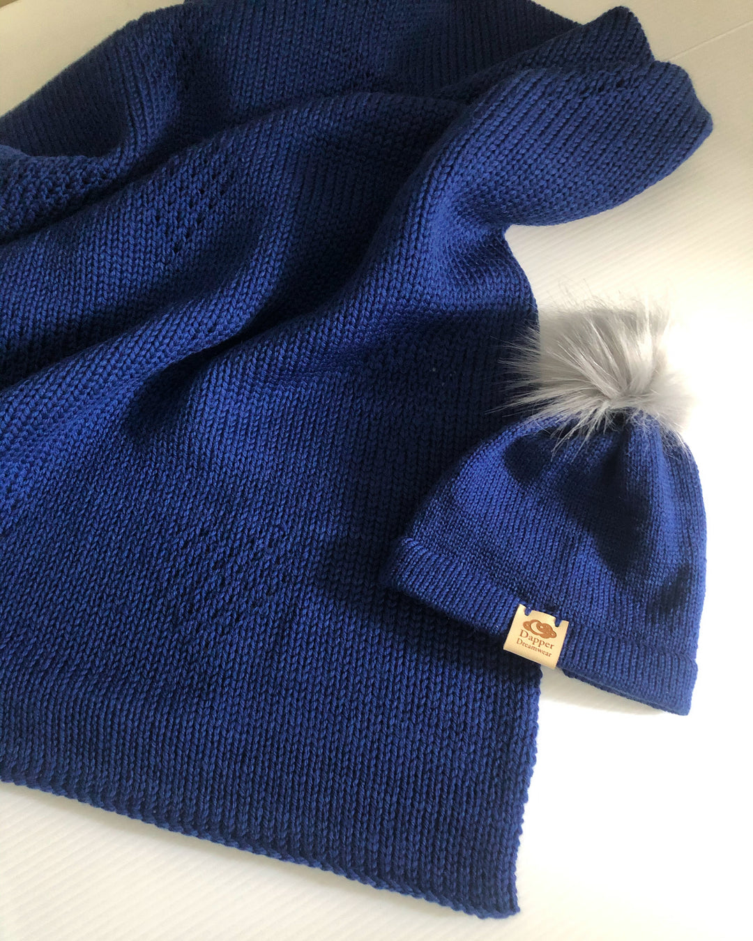 A merino wool cross with border leicester baby blanket and beanie with fluffy faux fur pom pom. Navy blue in colour with a textured love heart pattern. Baby gift set. Made in Australia from Australian grown wool. 